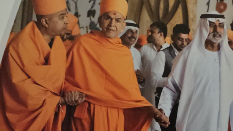 Two men in saffron robes, to their right a man in white dress--leading the central figure by the hand.