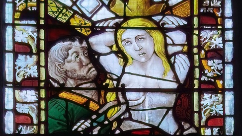 Stained glass window showing bare-chested woman, details obscured, and man holding cutting shears to her breast