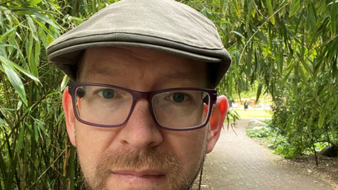Andrew Davison pictured wearing outdoor clothing and a hat, with greenery behind.