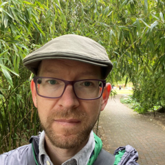Andrew Davison pictured wearing outdoor clothing and a hat, with greenery behind.