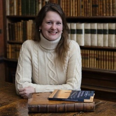 Marietta, seated at table in library setting