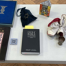 A table bearing objects including four books, a mosaic tile, a metal cup, folded paper cranes, and a candle holder.