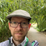 Andrew Davison pictured wearing outdoor clothing and a hat, with greenery behind.