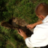 Viewed from behind, someone pulls up turf from grassland, as if excavating