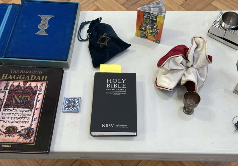 A table bearing objects including four books, a mosaic tile, a metal cup, folded paper cranes, and a candle holder.