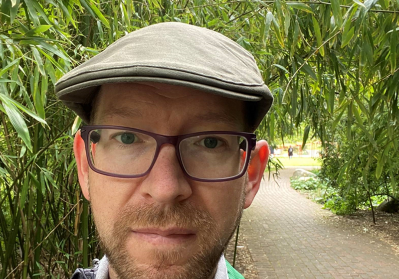 Andrew Davison pictured wearing outdoor clothing and a hat, with greenery behind.