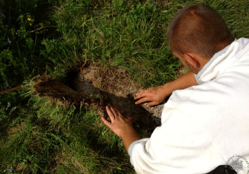 Viewed from behind, someone pulls up turf from grassland, as if excavating