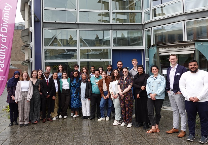 Small crowd facing the camera, facade of Faculty of Divinity behind