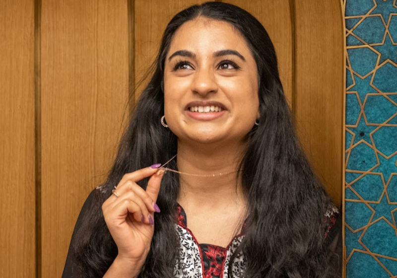 Close up photograph of Hina, gazing upward. To her right, an abstract design with gold stars on turquoise background.