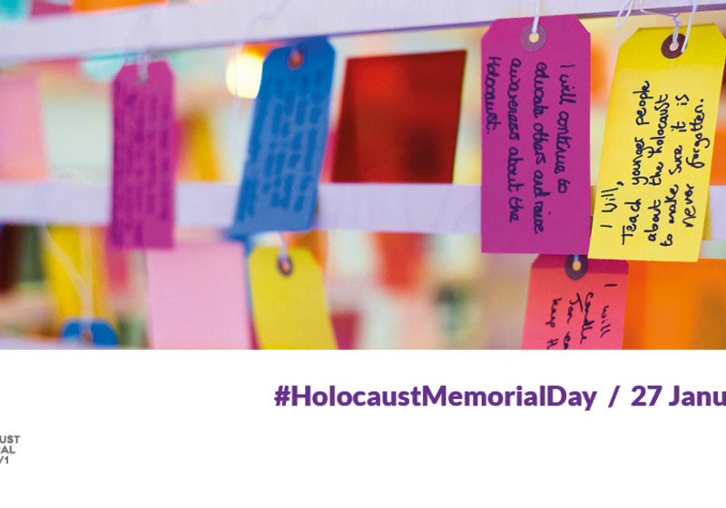 Colourful luggage tags hanging. Each has a handwritten message. Two pledges are legible: "I will, teach younger people about the Holocaust to make sure it is never forgotten. "I will continue to educate others and raise awareness about the Holocaust" 