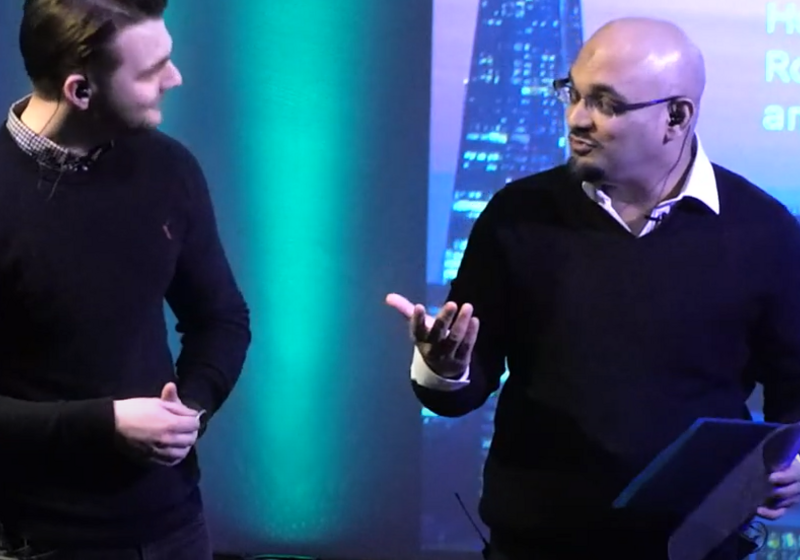 Two men in conversation, behind them a projector screen