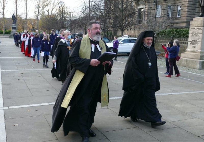 A procession of people in diverse religious garments walking towards a building 