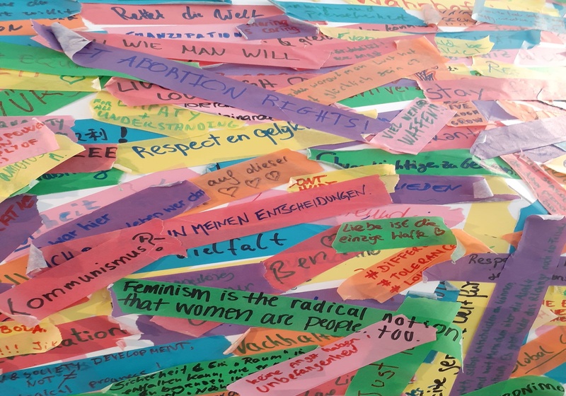 Strips of coloured paper with handwritten comments in German and English. Visible comments say "Kommunismus?" and "Feminism is the radical..."