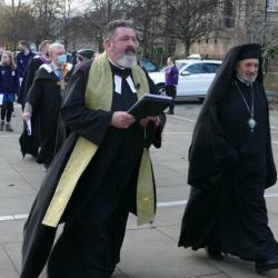 A procession of people in diverse religious garments walking towards a building 