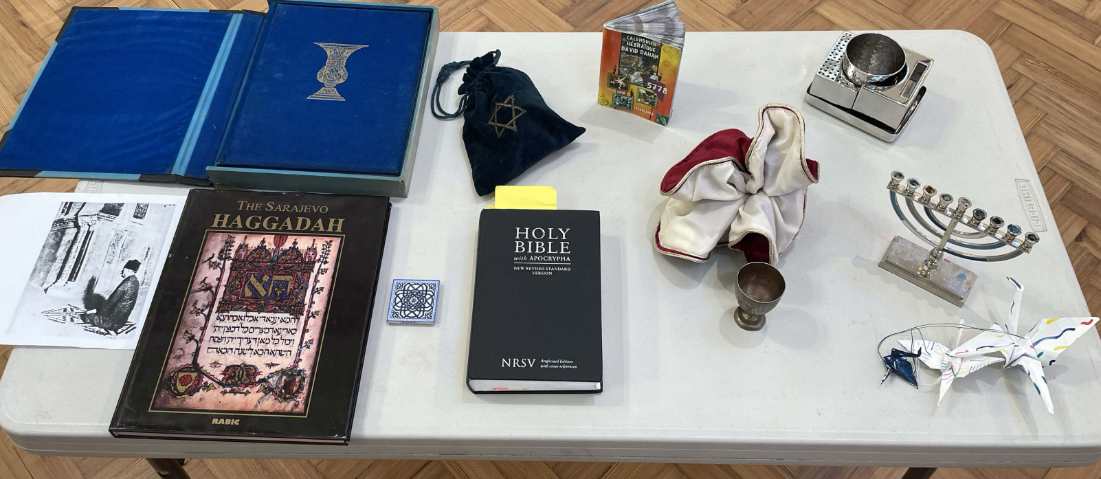 A display of boundary-crossing objects - photographed by Anastasia Badder for CIP (2023) A table bearing objects including four books, a mosaic tile, a metal cup, folded paper cranes, and a candle holder.
