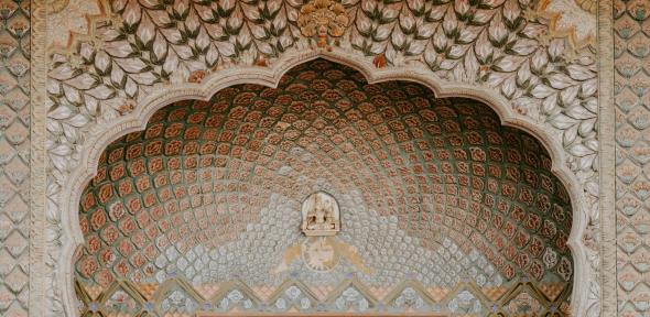 Featured image:Photograph of an ornate wooden door in Jaipur, India. Courtesy of Annie Spratt (2018) via Unsplash.com. A pale golden wooden door with a shell-like arch-pattern above it
