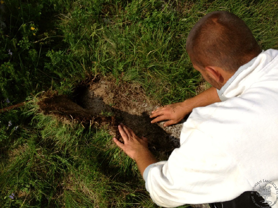 A Bosnian Landscapes image, courtesy of Dr Safet HadziMuhamedovic (2022) Viewed from behind, someone pulls up turf from grassland, as if excavating