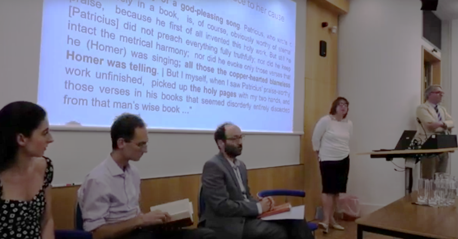 Still from the event livestream—CIP 2024. The three guests seated in front of a slide, Dr Lefteratou standing at lectern, Professor Van Kooten chairing questions.