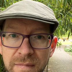 Andrew Davison pictured wearing outdoor clothing and a hat, with greenery behind.