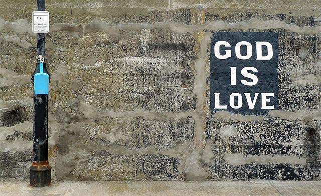 The words "God is love" painted on a grey wall near a lamppost.